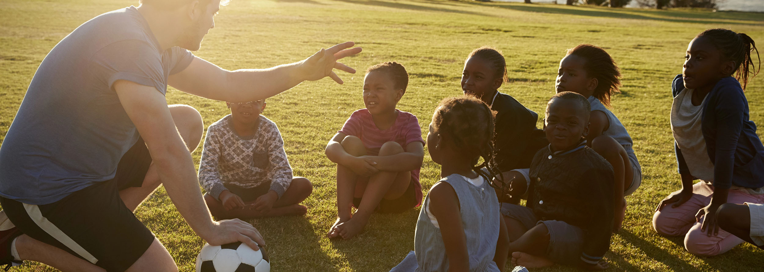 Elementary school kids and teacher sitting with ball in field